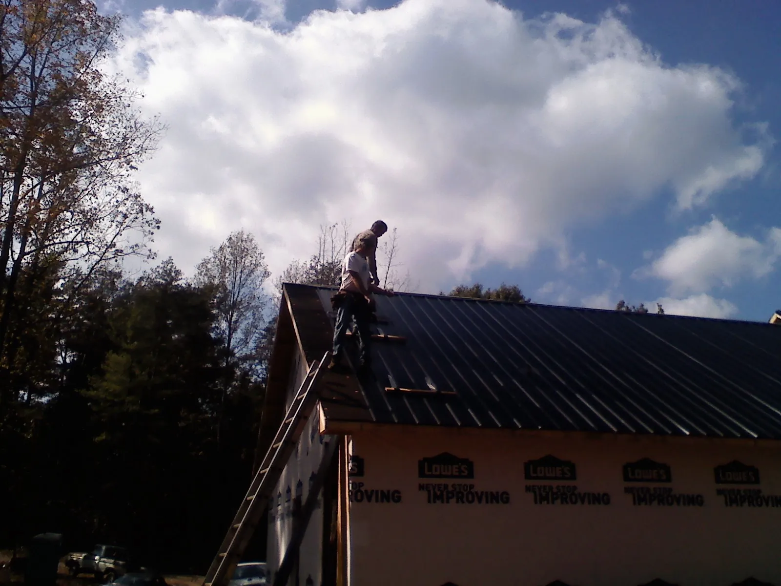 Roofer fastening dark metal panels high against a cloudy sky, from a Roof Inspection job in Bridgeport